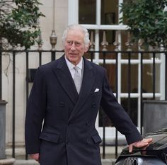 an older man in a suit and tie standing next to a car