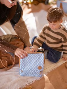 a young boy sitting on the ground next to a woman holding a blue and white purse