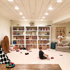 a young boy sitting on the floor in front of a book shelf filled with toys