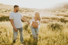 a pregnant woman holding the hand of a man in an open field with tall grass