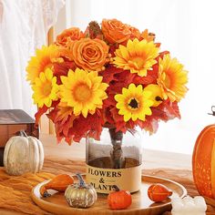 a vase filled with yellow and orange flowers on top of a table next to pumpkins