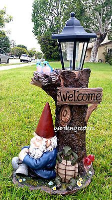 a garden gnome sitting next to a welcome sign