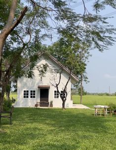 a white house sitting in the middle of a lush green field next to a tree