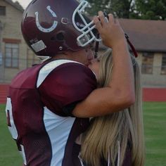 two girls in football uniforms embracing each other on the field with houses in the background