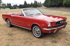 an old red mustang convertible parked in a field