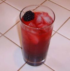 a glass filled with ice and blackberries on top of a tiled floor