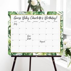 a calendar on a easel with flowers and greenery in the background, says guess baby charlotte's birthday