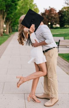 a man and woman kissing on the cheek while holding a graduation cap over their head