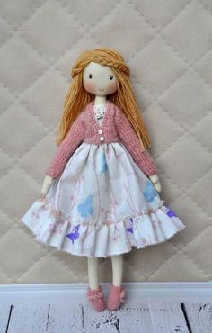 a doll with red hair wearing a white dress and pink shoes standing next to a quilted wall