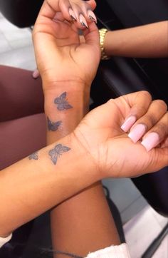 two women holding hands with tattoos on their wrists and fingers, both wearing matching bracelets