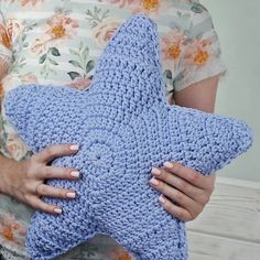 a woman holding a blue crocheted star pillow in her hands, with one hand on it