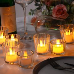 candles are lit on a table with wine glasses and utensils next to it