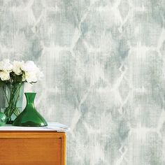 two vases with white flowers sit on a table in front of a wallpapered background