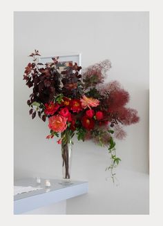 a vase filled with red flowers on top of a white table next to a mirror