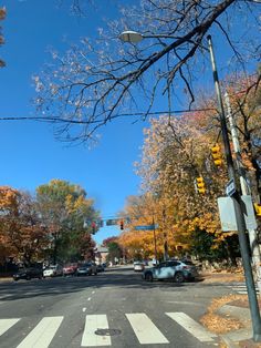 an empty street with cars parked on the side and trees lining the road in autumn