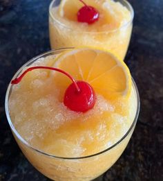 two glasses filled with pineapple and cherries on top of a black countertop