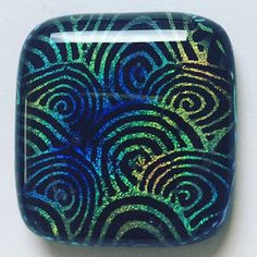 a blue and green square shaped object on a white surface with swirls in the center