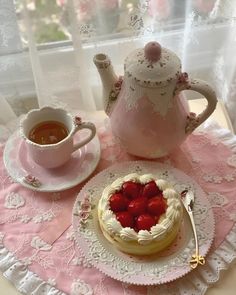 a cake with strawberries is on a table next to a teapot and cup