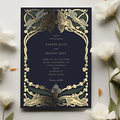 a wedding card with gold foil on it and flowers in the background, along with some white tulips