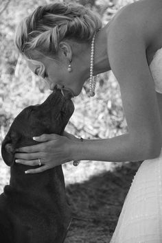 a woman in a wedding dress kissing a dog's face with her mouth open