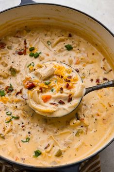 a ladle full of chicken chowder soup with cheese and green onions in it