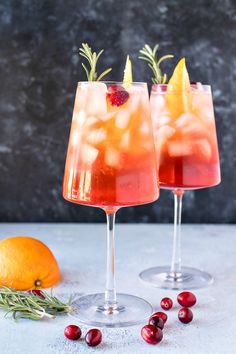 two glasses filled with cranberry lemonade and rosemary garnish next to an orange