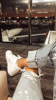 a person's feet with ripped jeans and white tennis shoes in an airport terminal