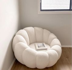 a white chair sitting in front of a window next to a book on a wooden floor