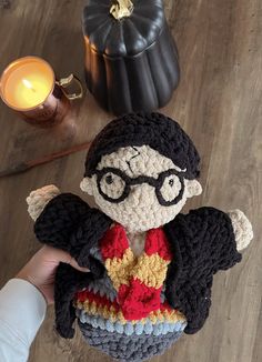 a crocheted harry potter doll sitting on top of a table next to a candle