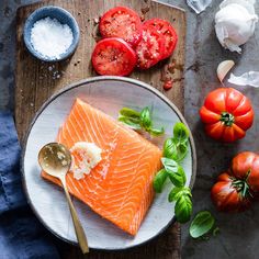 raw salmon on a plate with tomatoes, garlic and seasoning next to the fish