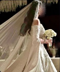 a woman in a white wedding dress holding a bouquet of flowers and wearing a veil