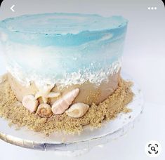 there is a blue and white cake with shells on the top, surrounded by sand