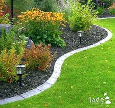 a garden with lots of flowers and plants around it, along with some lights in the grass