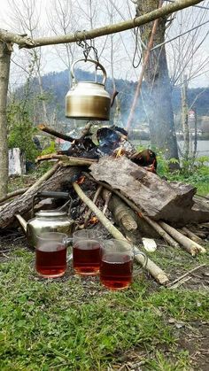 tea pots sitting on top of a pile of wood next to a fire