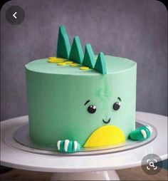 there is a green cake with a dinosaur on it's face and trees on top