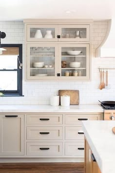 a white kitchen with wooden floors and cabinets in front of a window that is open to the outside