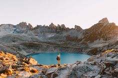 two people standing on top of a mountain next to a lake