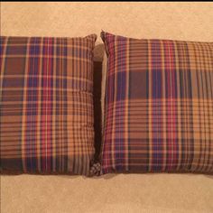 two brown and blue plaid pillows sitting on top of a carpeted floor next to each other