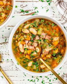 two bowls filled with soup on top of a white wooden table next to gold spoons