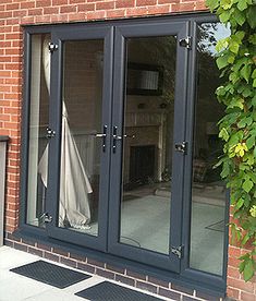 a brick building with black double doors and glass windows on the outside, in front of a green tree