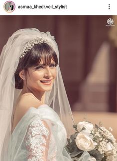 a woman in a wedding dress holding a bouquet and smiling at the camera while wearing a veil over her head