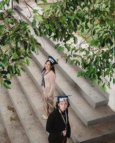 two women in native garb standing on steps under a tree and looking at the camera