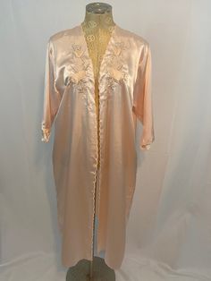 "Vintage 1980s or earlier light pink silk robe by Komoda. Details include embroidered pink and light green flowers on the front bodice and on end of sleeves. Robe does not have a sash or loops for a sash, so robe does not close. There are no rips, stains, tears, holes, or snags as far as I can tell.  Brand is Komoda. Size is XXL. No materials tag, but material is silky- most likely polyester or actual silk. Please refer to my measurements below! Giselle the dress form measurements: 47\" bust  48\" waist 50\" hips 18\" shoulders 11.5\" sleeve length 43\" length (shoulder seam to hem) 33\" length (armpit to hem) Please feel free to message me with any questions, concerns, or any other measurements! Thank you!" Elegant Long Pink Robe, Silk Robe Long Vintage, Long Pink Silk Robe, Luxury Pink Women's Robe, Light Green Flowers, Pink Silk Robe, Long-sleeved Pink Vintage Robe, Silky Robe, Printed Tunic Dress