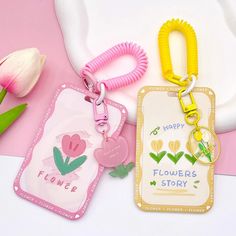 two keychains with flowers on them are next to a flower tag and tulips