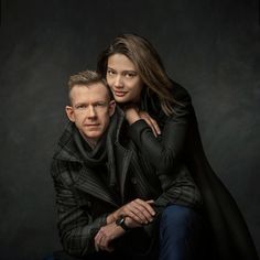 a man and woman are posing for a portrait in front of a dark background with their arms around each other