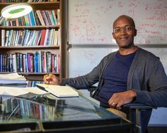 a man sitting at a desk in front of a book shelf with books on it