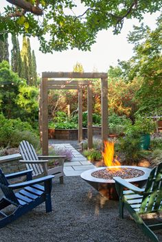 an outdoor fire pit surrounded by lawn chairs and graveled area with trees in the background