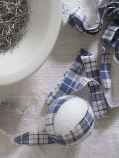 a white bowl and some silver pins on a table cloth with a blue plaid ribbon next to it