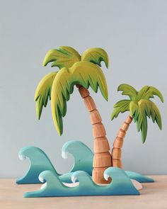 two wooden palm trees sitting on top of a table next to waves and the ocean