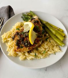 a white plate topped with pasta and meat covered in sauce next to asparagus